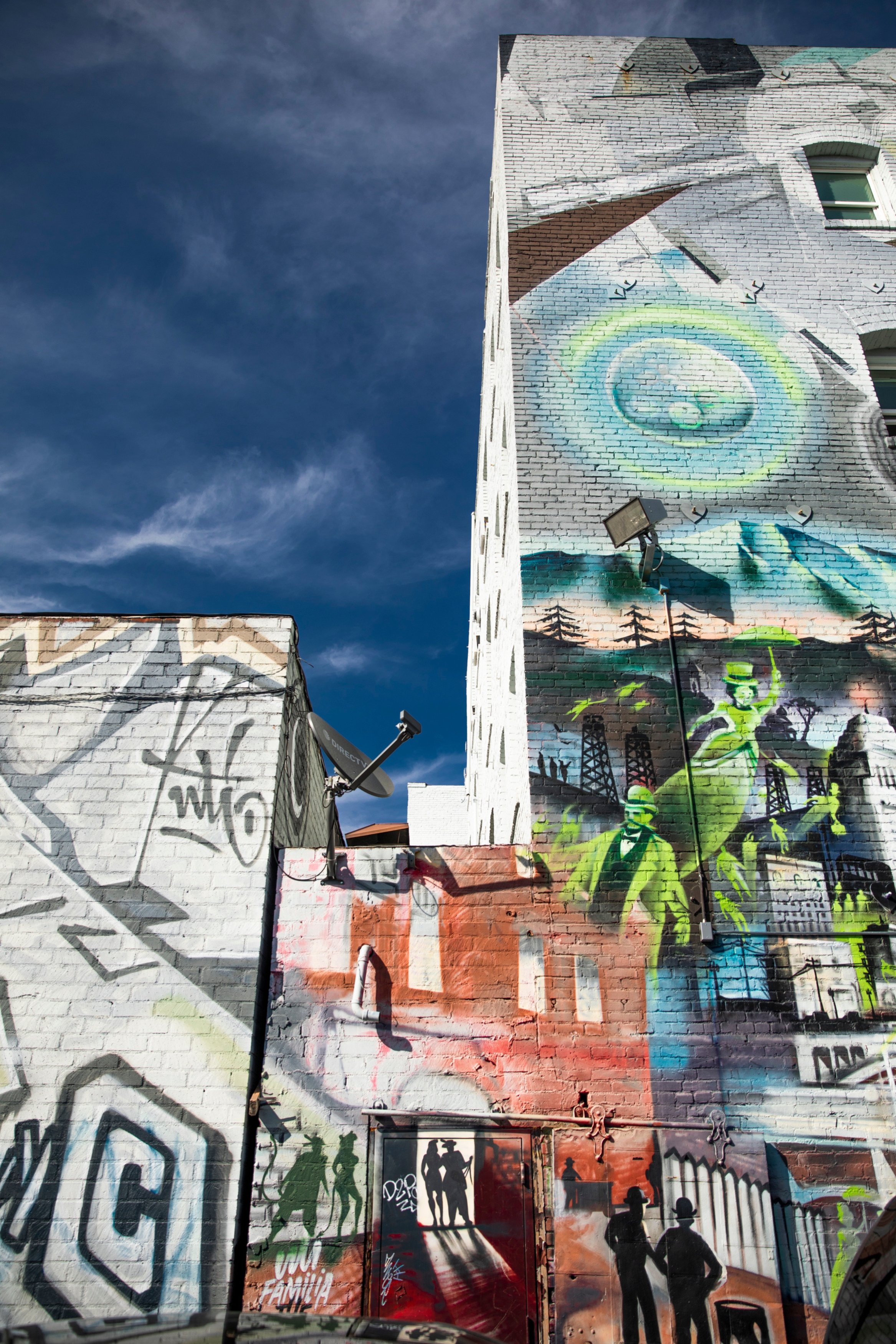 A colorful mural on a brick wall under a blue sky with clouds.