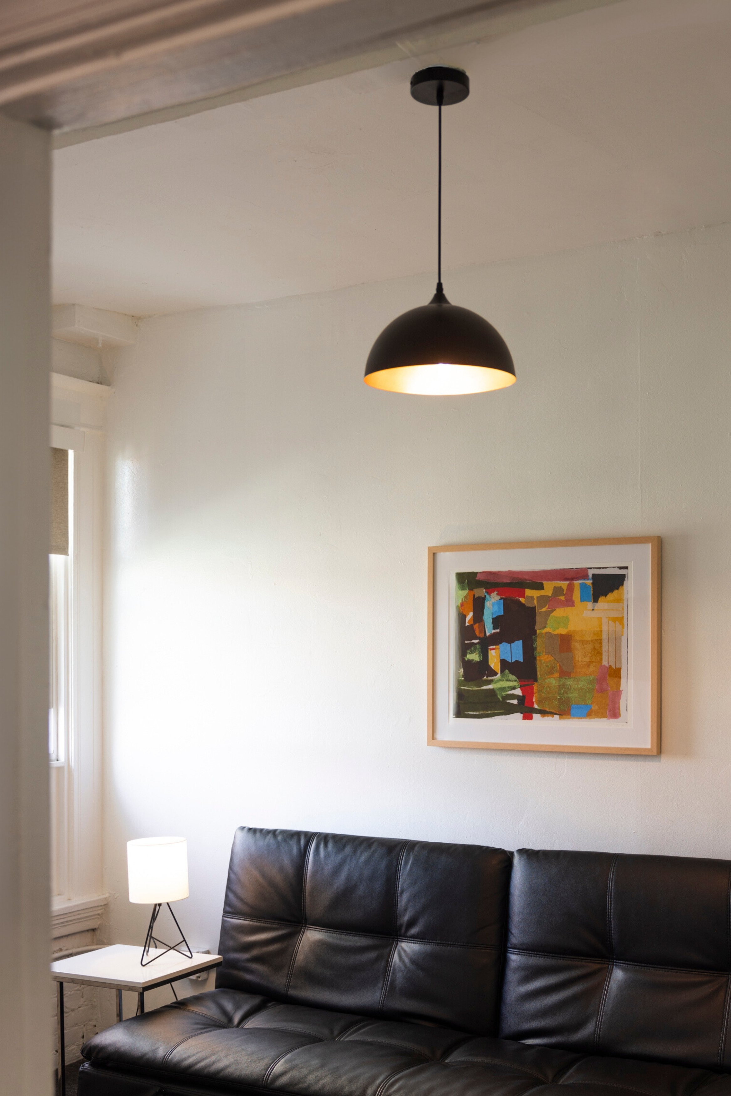A small seating area with a black leather sofa, a side table, and abstract art on the wall.