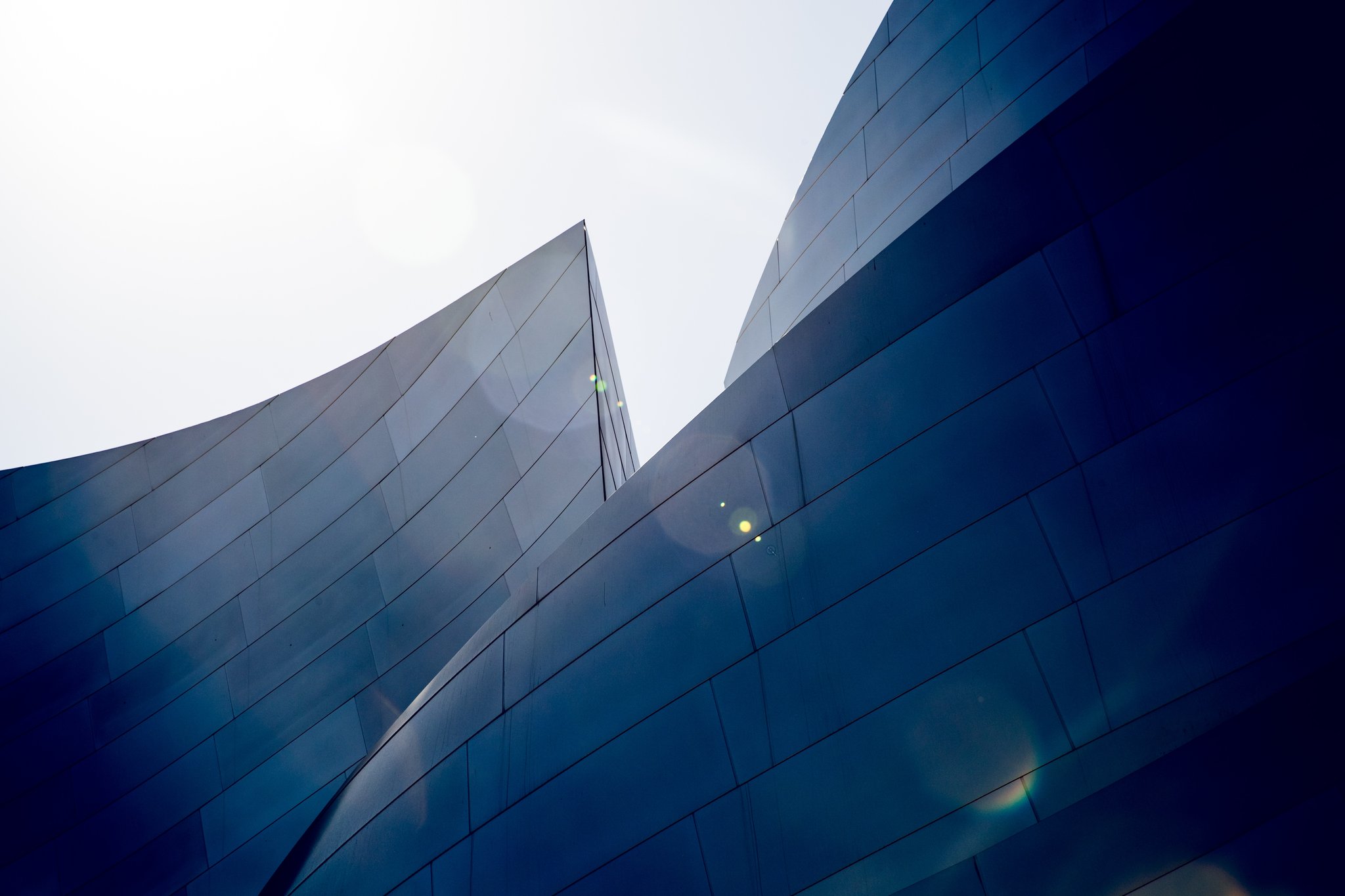A close-up of a building's blue glass exterior with curved facets reflecting the sky.