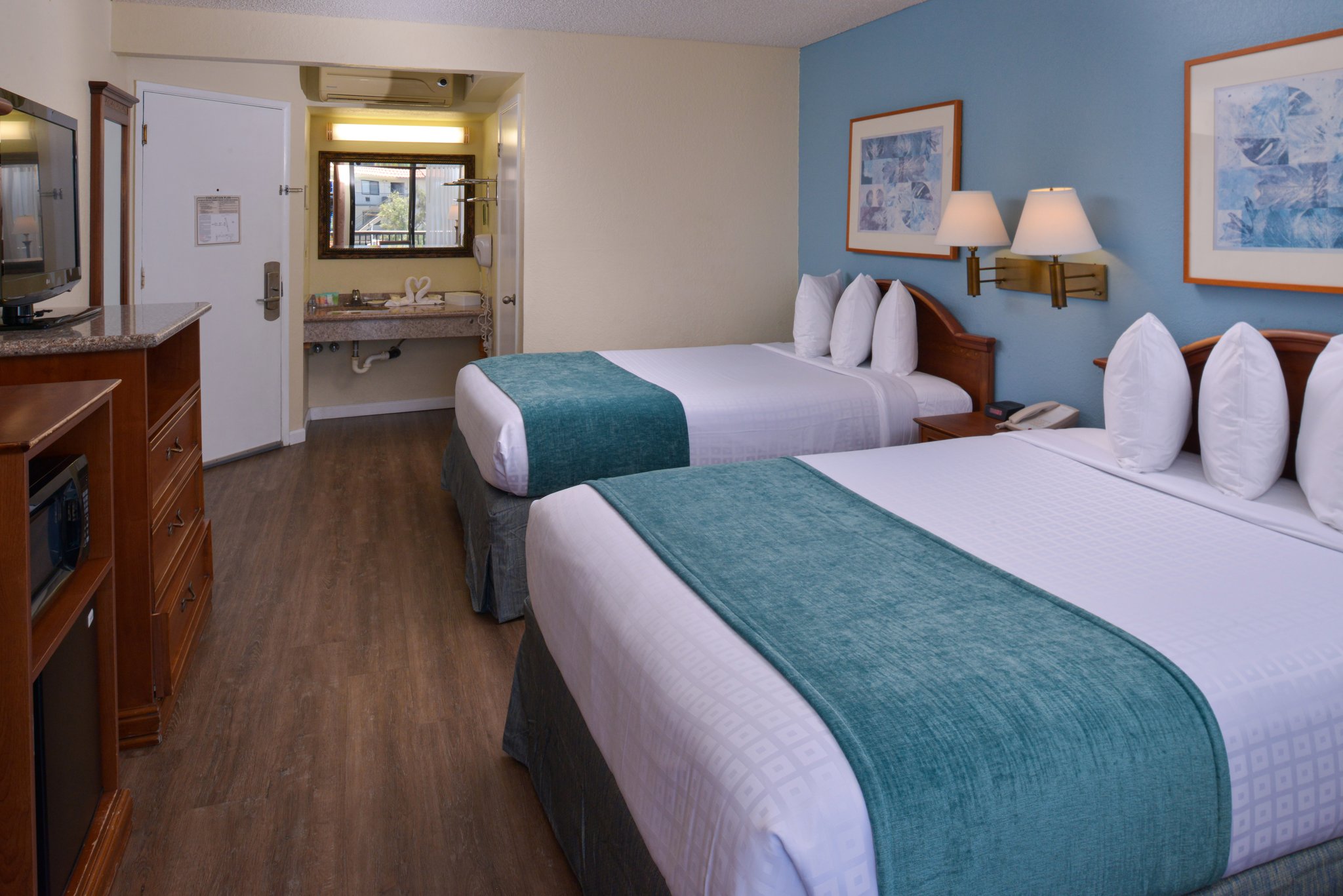 A hotel room with two beds, a TV, and a bathroom in the background.