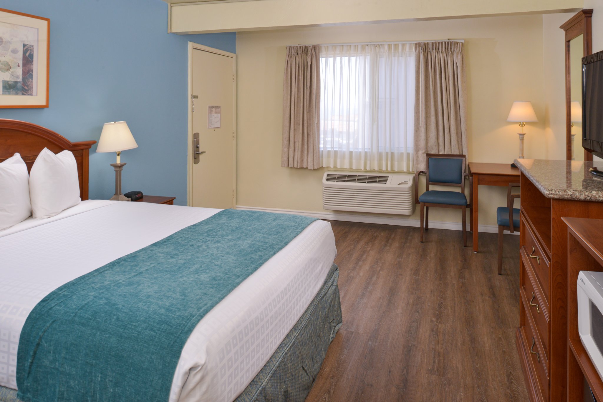 A hotel room with a queen bed, desk, TV, and window.