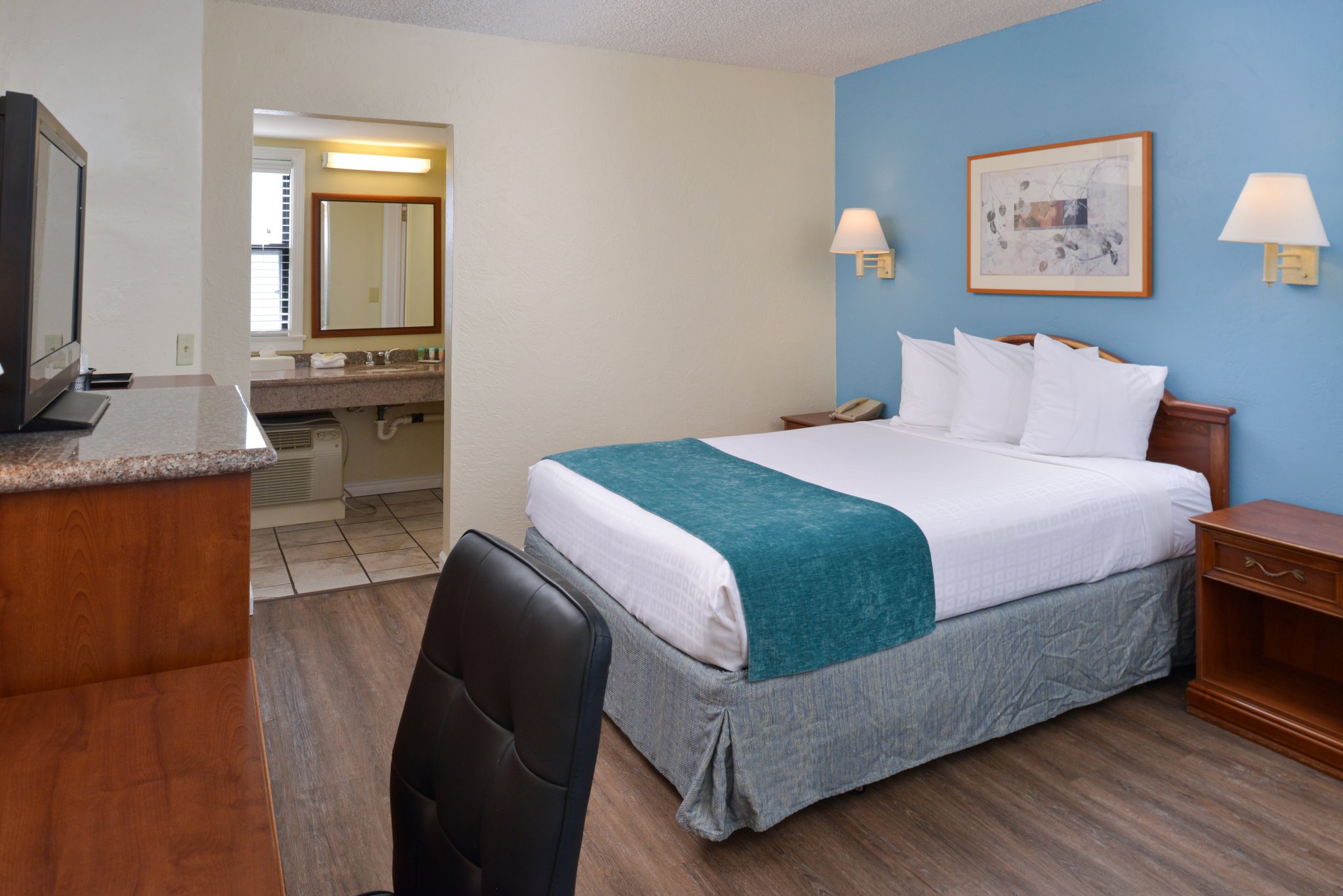 A hotel room with a bed, desk, TV, and bathroom in the background.