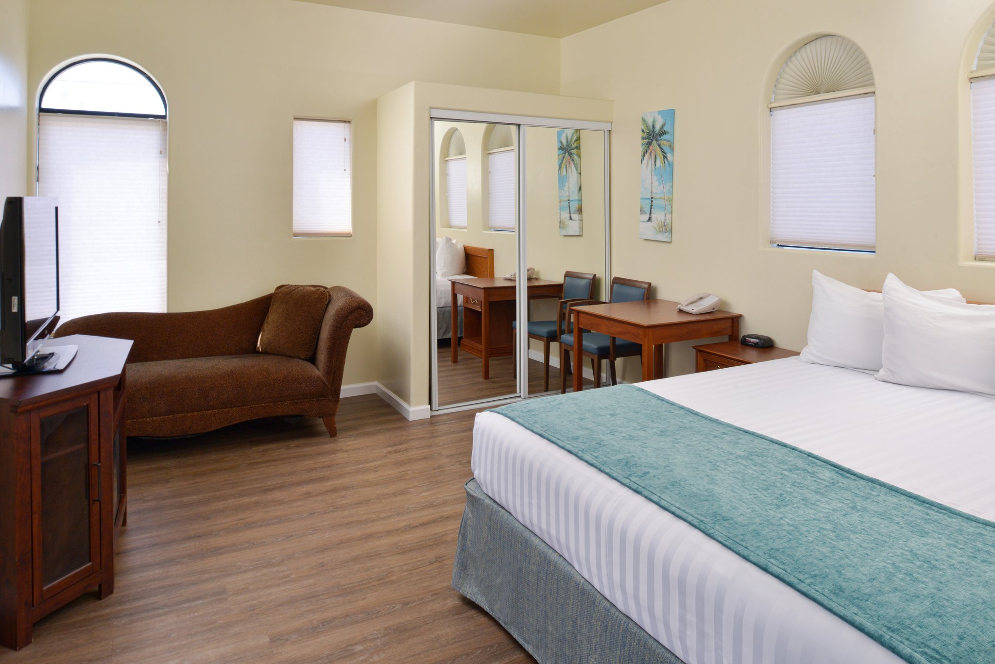 A wide view of a hotel room with a large bed, desk, sofa, and mirrored closet