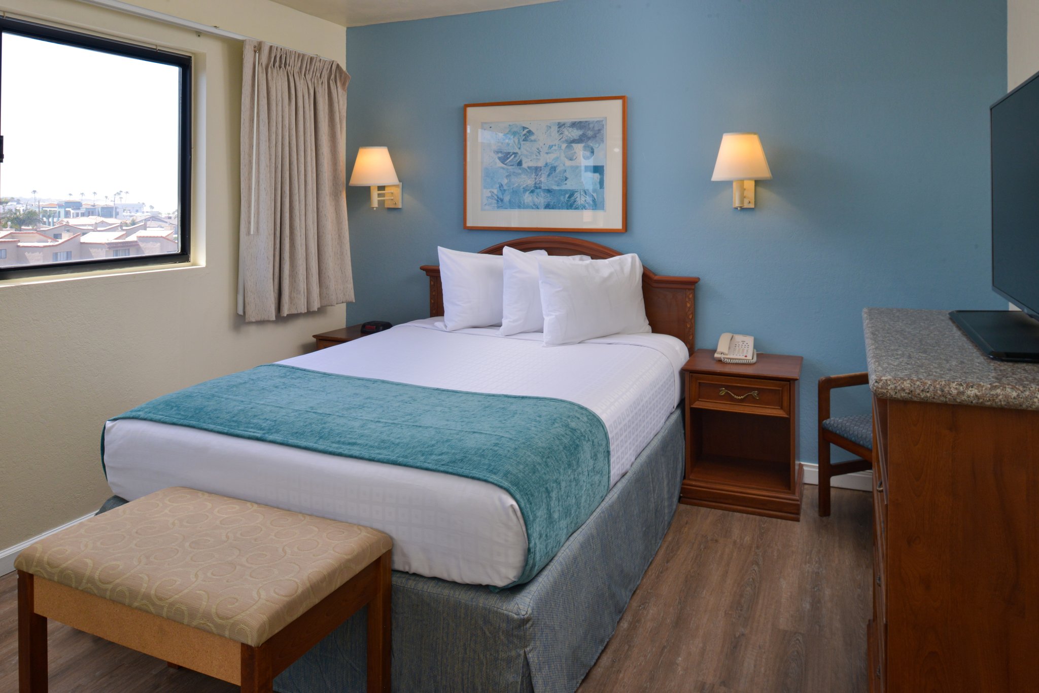 A hotel room with a bed, nightstand, TV, and window